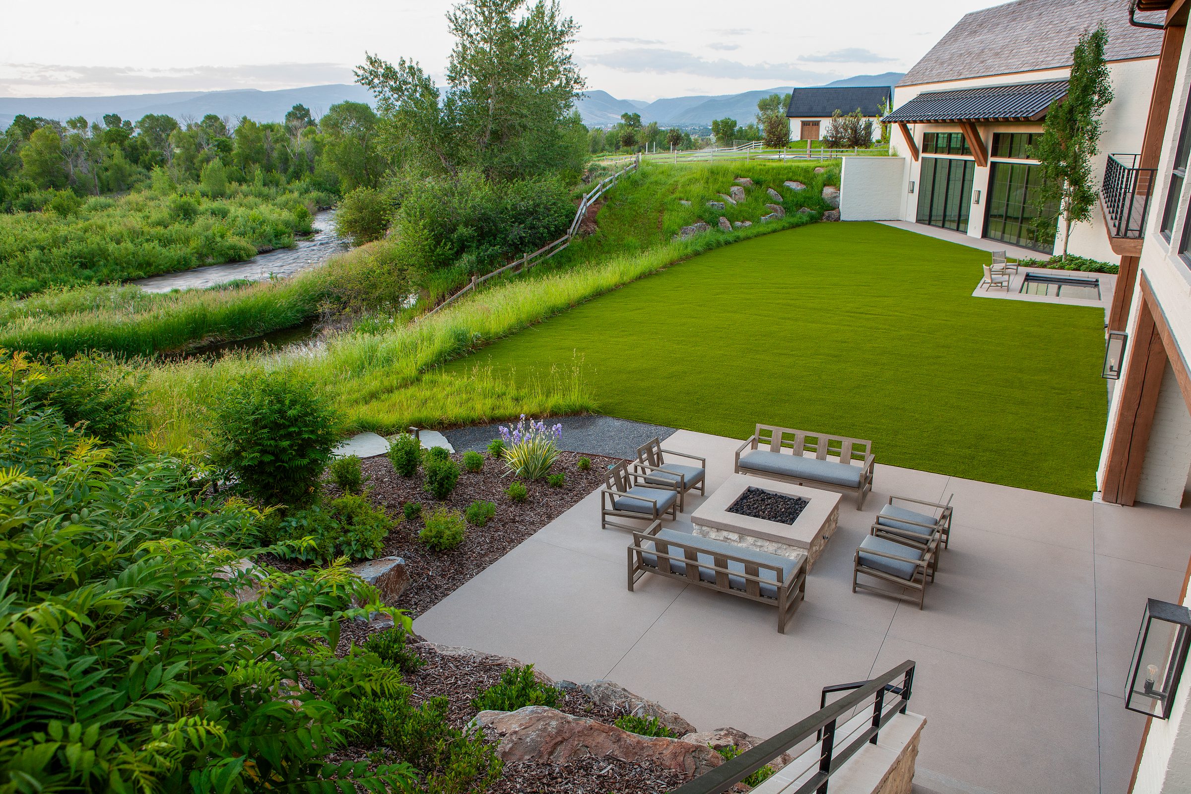 Modern patio overlooking lush green lawn and stream.