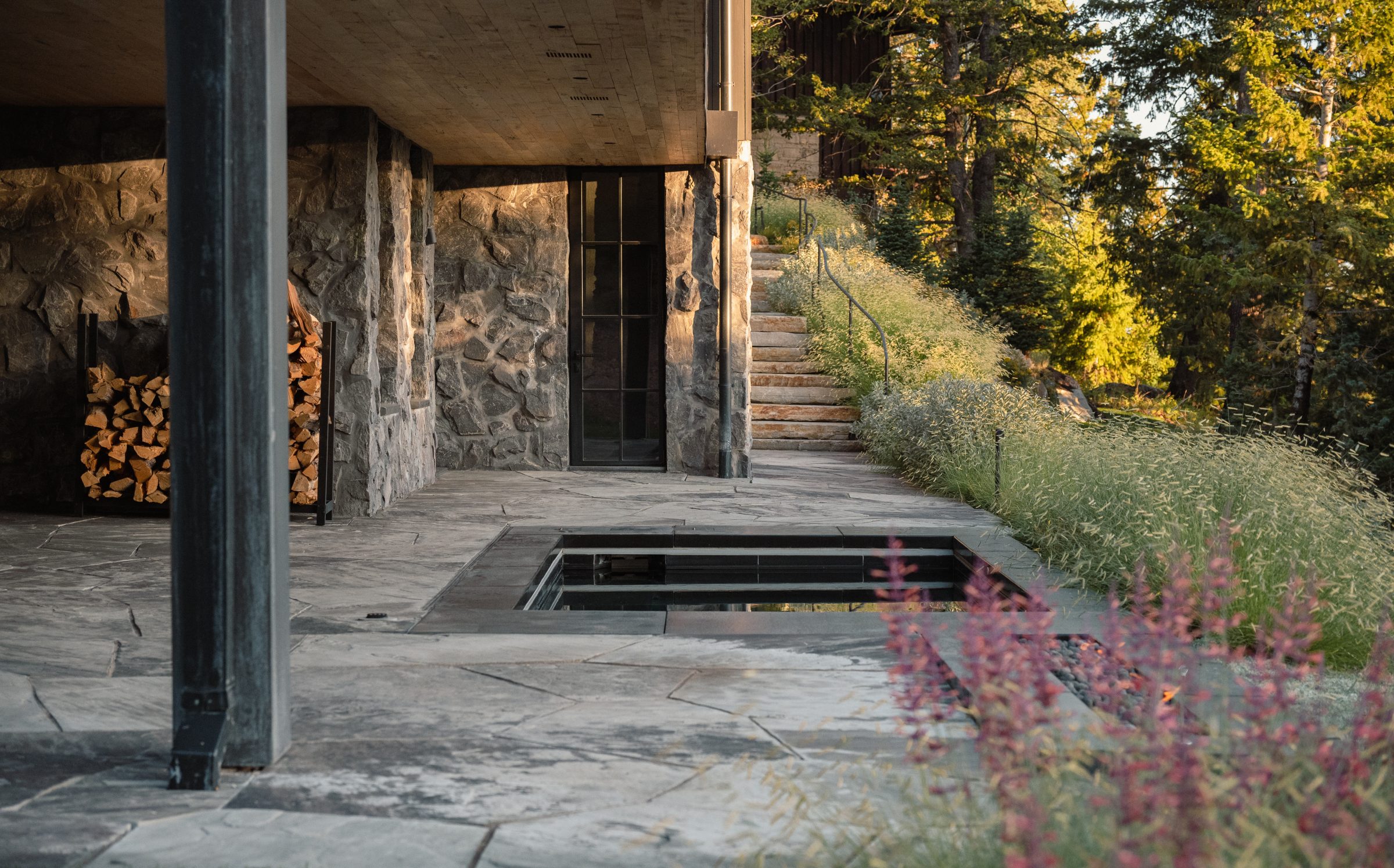 Stone patio with firewood and lush outdoor scenery.