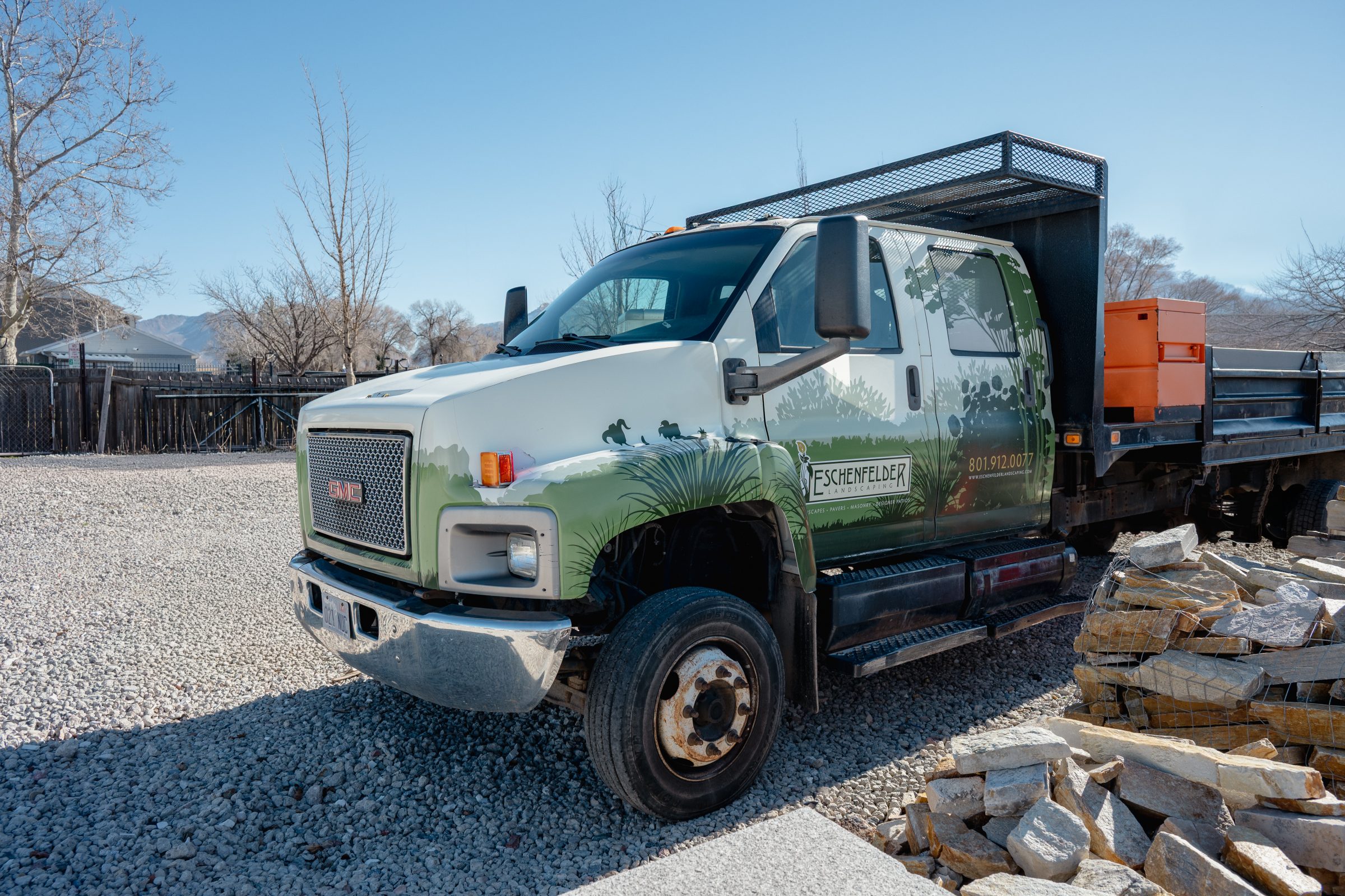 Landscaping truck in gravel area with stone pile.
