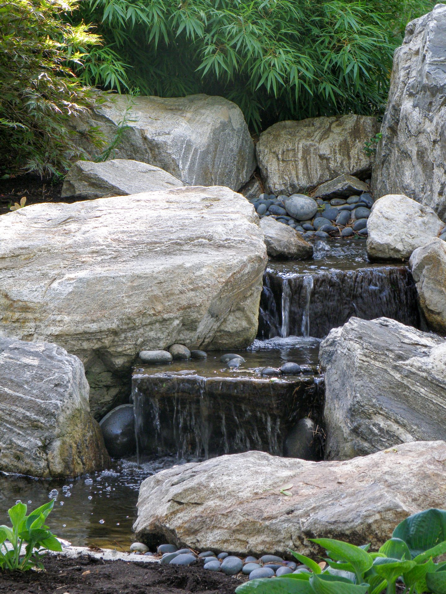 Serene garden waterfall with rocks and greenery.